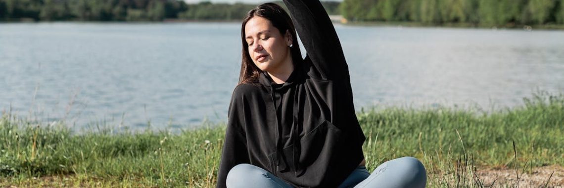 Woman enjoying a relaxing yoga session by a scenic lakeside. Perfect outdoor wellness setting.